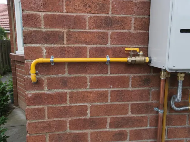Yellow gas pipe and valve mounted on a brick wall beside an outdoor unit in Belfield